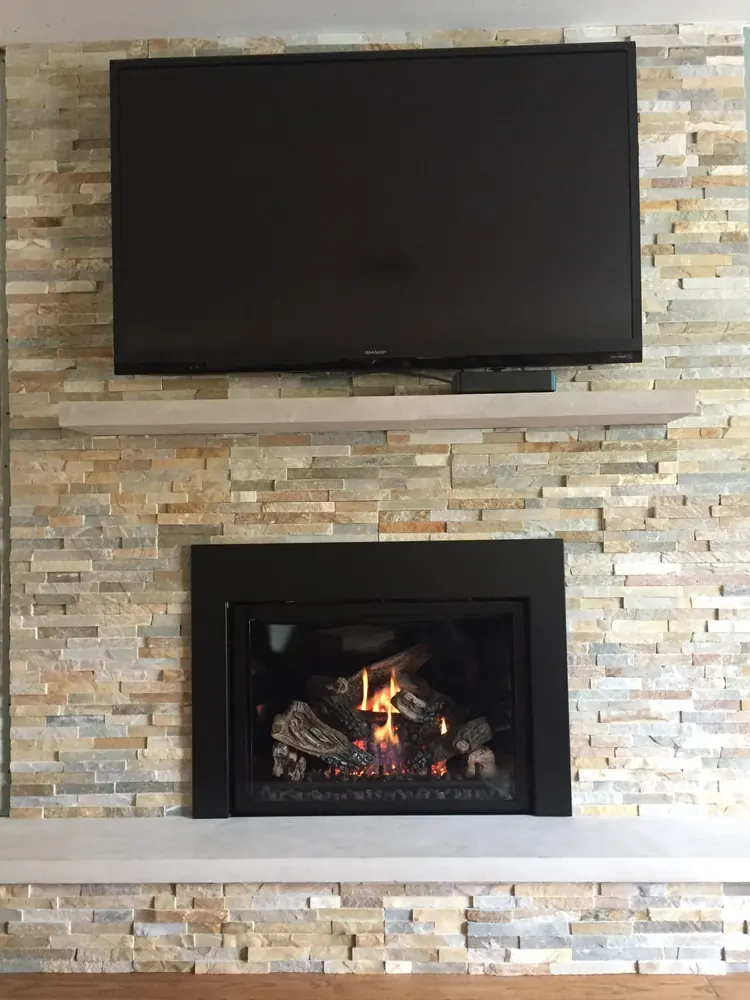 A gas insert in a split-face ledgestone wall beneath a wall-mounted TV