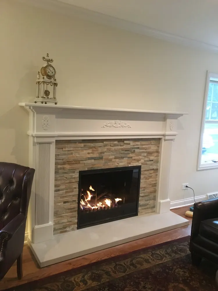 A gas fireplace burning in a white mantel with a stone surround — one of our installs