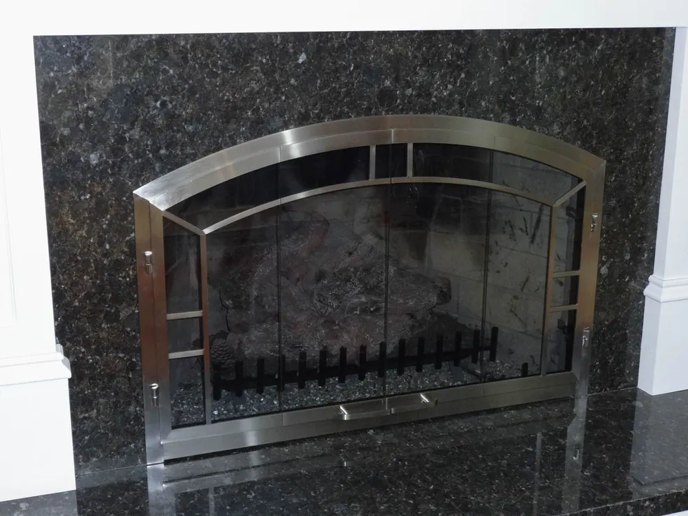 A renovated fireplace with polished granite and custom glass doors